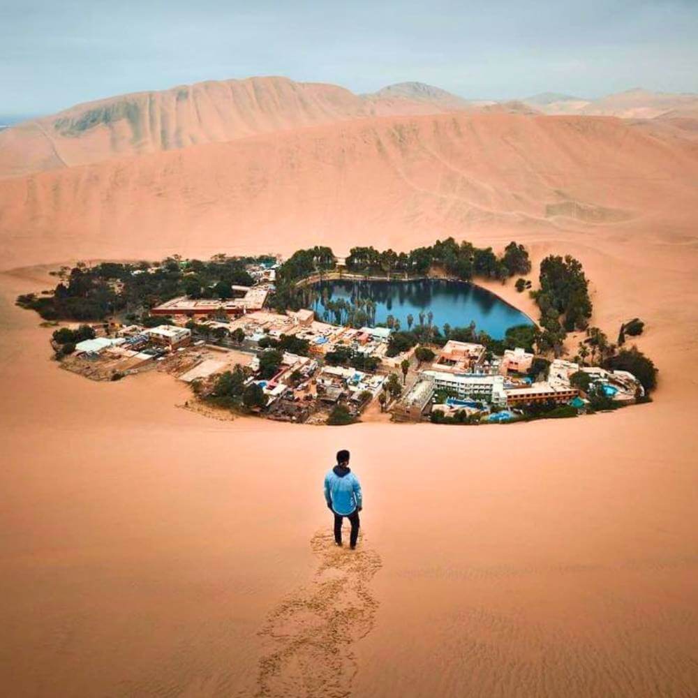 Traveler overlooking the Huacachina Oasis surrounded by giant sand dunes in the Peruvian desert.