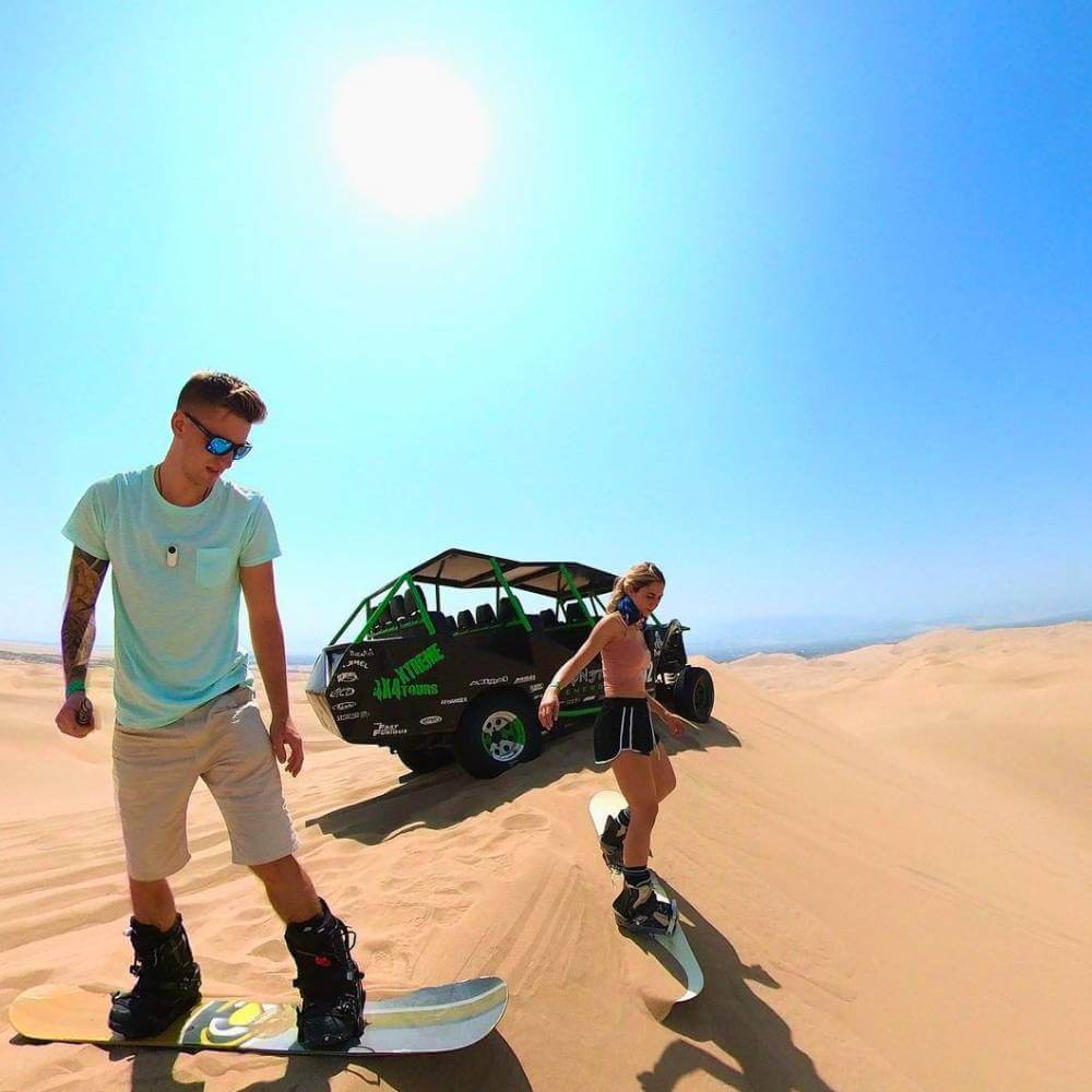 Tourists practicing sandboarding on the giant dunes of Huacachina during a desert adventure tour from Lima.