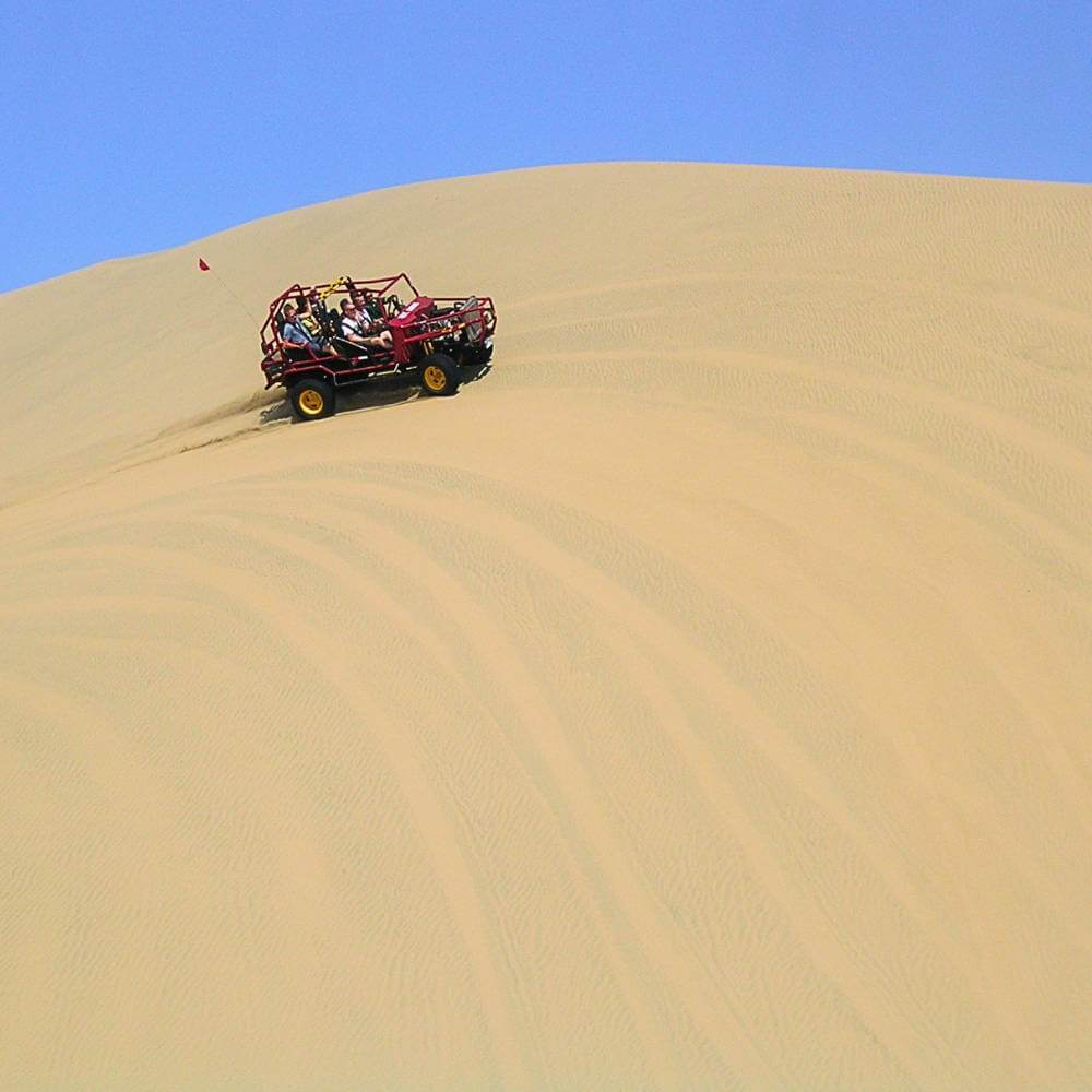 Travelers enjoying an exciting dune buggy ride across the massive sand dunes of Huacachina near Ica, Peru.