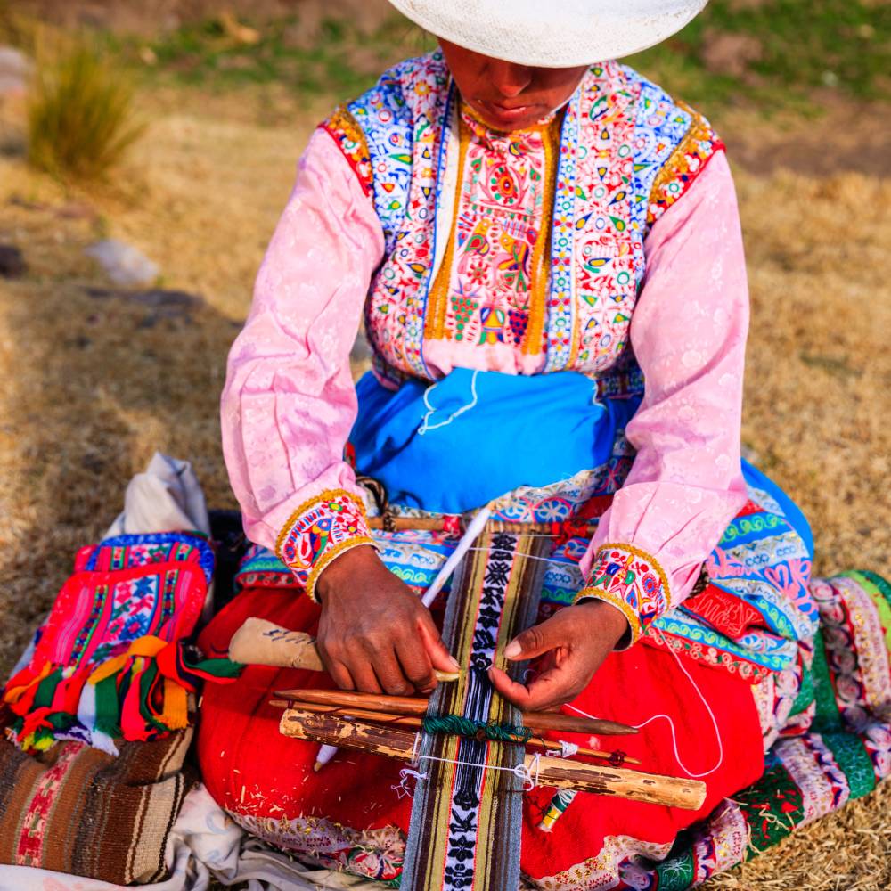 Local woman in traditional Andean clothing weaving colorful textiles in Chivay during the Colca Canyon Tour and Trip to Puno.