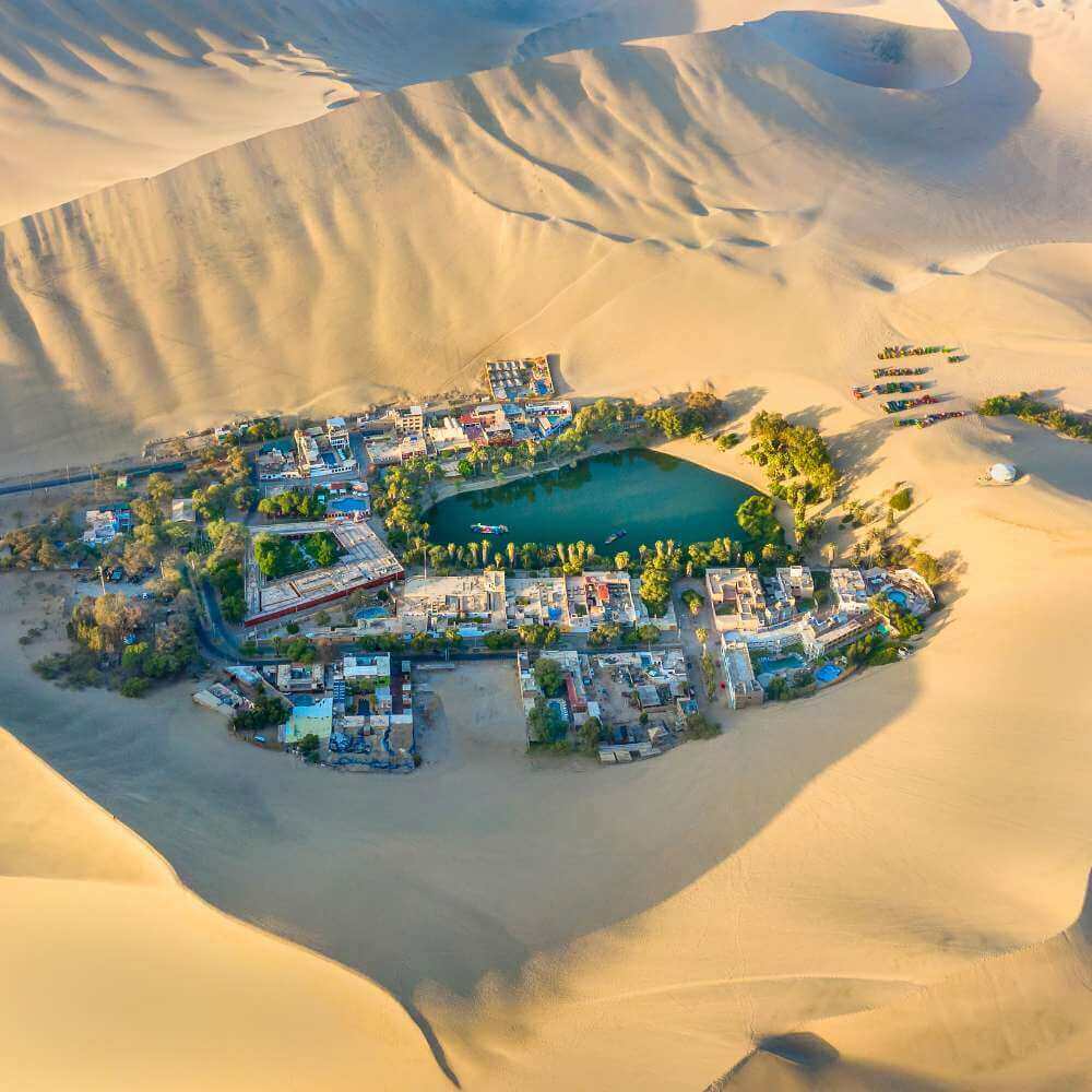 Aerial view of Huacachina Oasis surrounded by giant sand dunes in the Ica Desert, Peru.