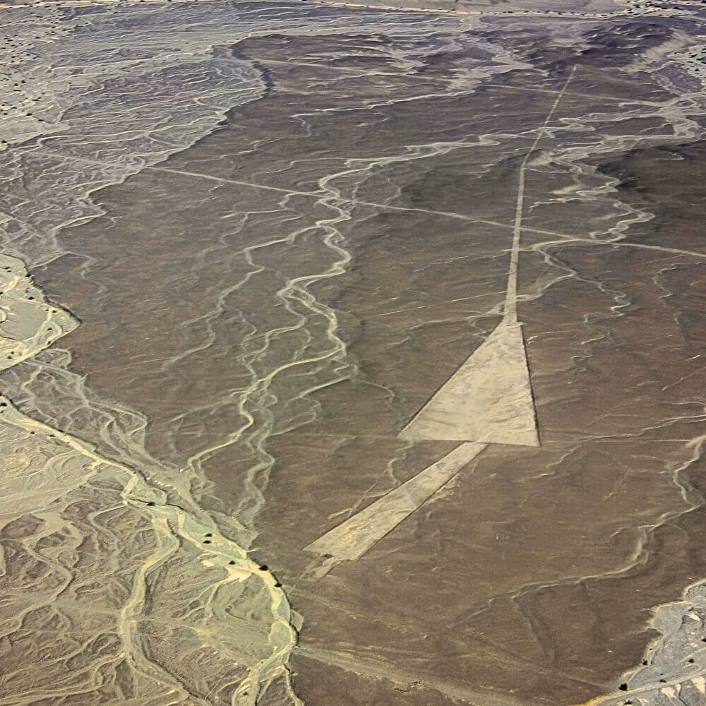 Aerial photograph of a giant arrow-shaped geoglyph among the Nazca Lines in the Peruvian desert.