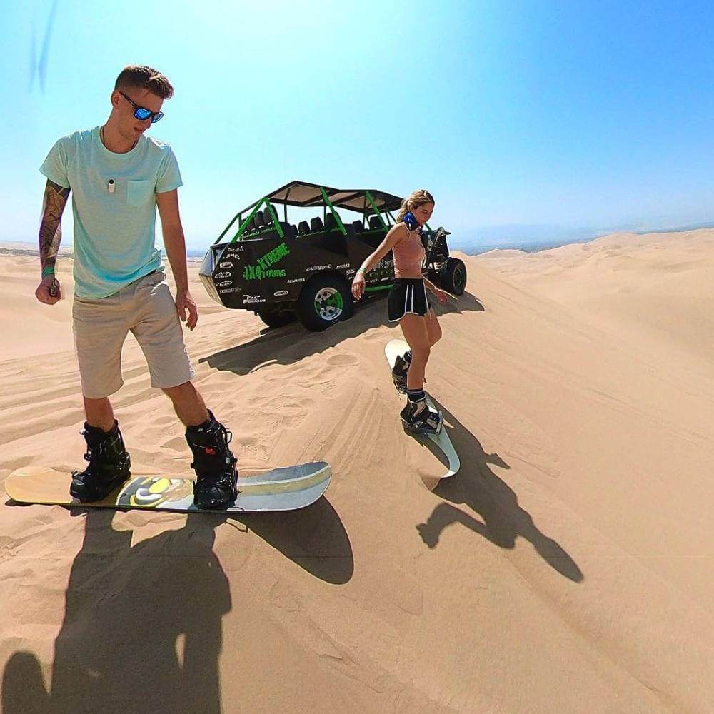 Reisende genießen das Sandboarding auf den hohen Dünen von Huacachina während eines Dune Buggy-Abenteuers in Peru.