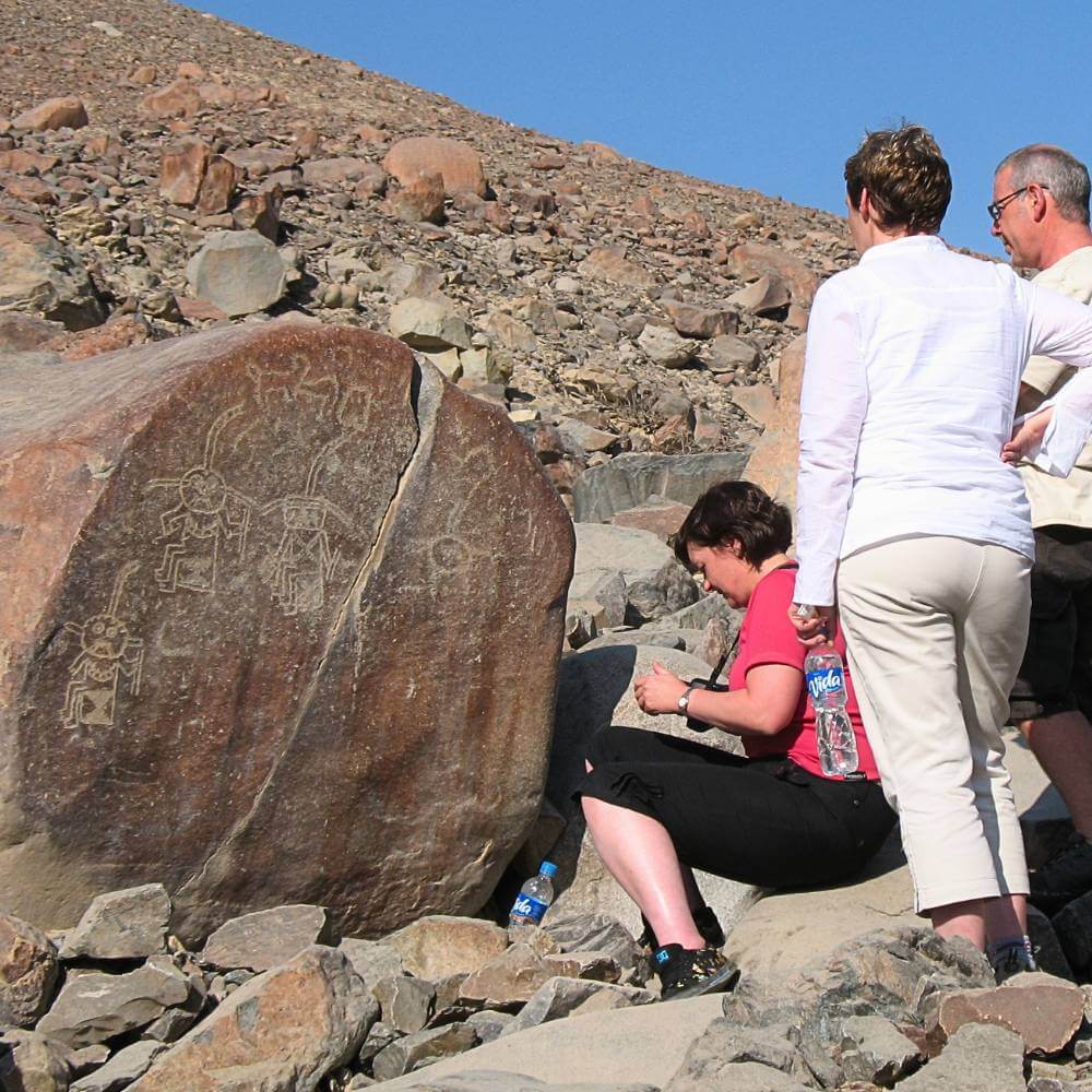 Viaggiatori che esplorano antichi petroglyphs scolpiti in massi vulcanici presso il sito archeologico di Chicchitara vicino a Nazca, Perù.