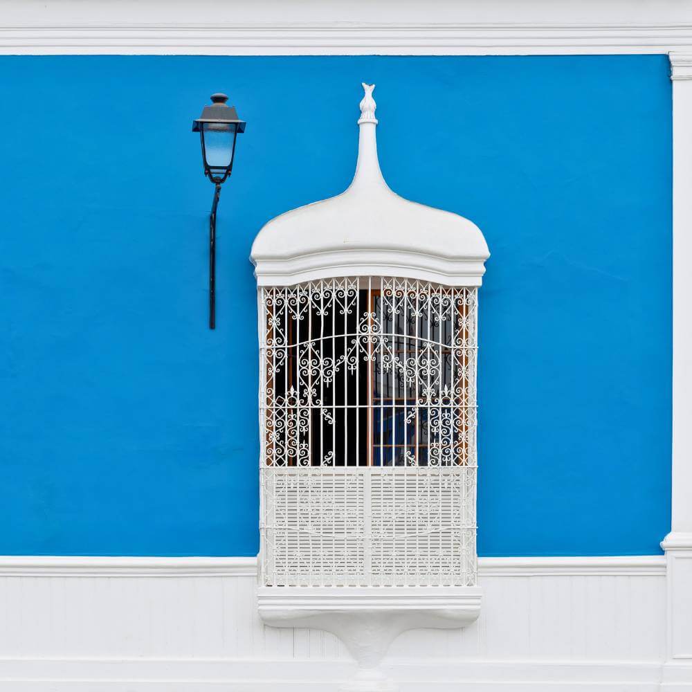 Casa Urquiaga, a Colonial Jewel. Ornate white colonial balcony set against a vivid blue façade in the historic center of Trujillo, Peru.